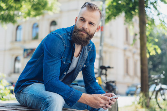 Young bearded man in denim shirt sitting on bench