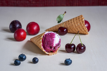Homemade ice cream in a waffle cone with berries on wooden background. Plum, blueberry, cherry. Soft focus.