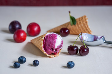 Homemade ice cream in a waffle cone with berries on wooden background. Plum, blueberry, cherry. Soft focus.