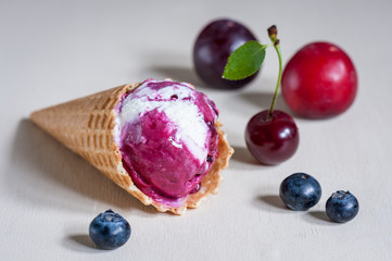 Homemade ice cream in a waffle cone with berries on wooden background. Plum, blueberry, cherry. Soft focus.