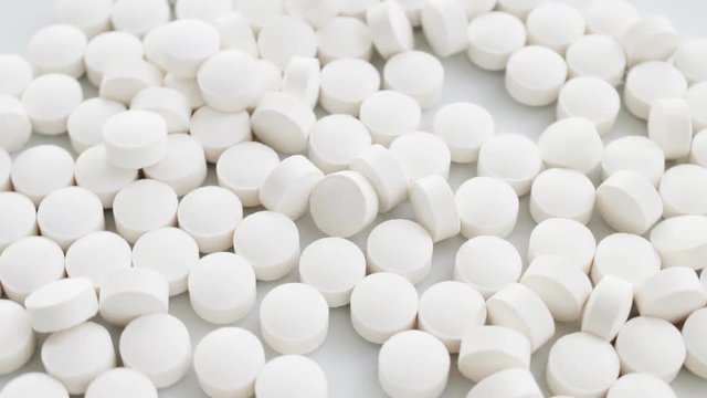 White tablets, pills slow rotation, closeup, white background. Concept of 	pharmaceuticals; meds, drugs, 	pharmacology, materia medica. Closeup.