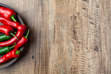 Red and green chilli pepper in a dish on wooden table with copy space