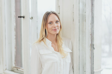 Blonde cheerful woman standing by window at home