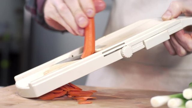 Tracking shot of chef slicing carrot using mandolin