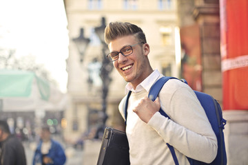 Smiling student with backpack and laptop.