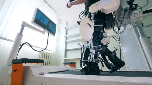Physically challenged person is training his legs on a running track. Electronic medical robotic for rehabilitation.