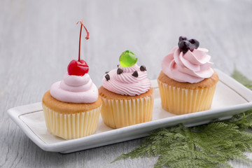 Pink cupcake with red cherry,blueberry sauces,green jelly and chocolates on wood.Copy space.