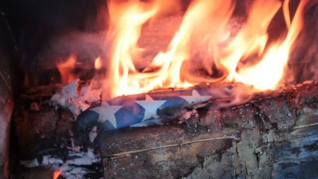 Flames bursting from on top of an American flag being burnt out of respect.