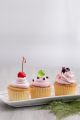 Pink cupcake with red cherry,blueberry sauces,green jelly and chocolates on wood.Copy space.