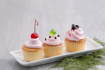 Pink cupcake with red cherry,blueberry sauces,green jelly and chocolates on wood.Copy space.