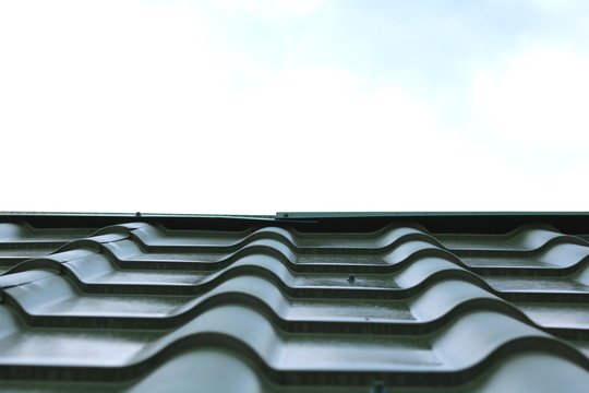 New green roof of house made of iron shingles against blue sky background closeup