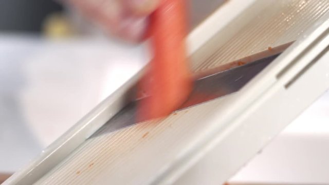 Close-up shot of chef slicing fresh carrot using mandolin