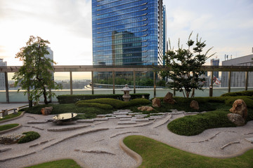 Small Japanese rooftop rock garden surrounded by green grass and bushes in city center