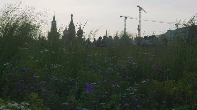View of people sitting on grass of grassplot with Kremlin and building crane on background in evening