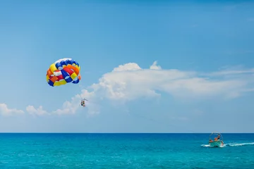 Tuinposter Watersport Mensen vliegen aan een kleurrijke parachute getrokken door een motorboot