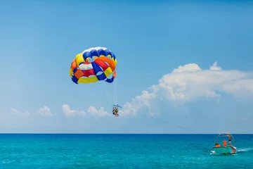 Fotobehang Watersport Mensen vliegen aan een kleurrijke parachute getrokken door een motorboot