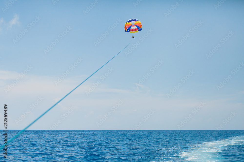 Wall mural People flying on a colorful parachute towed by a motor boat