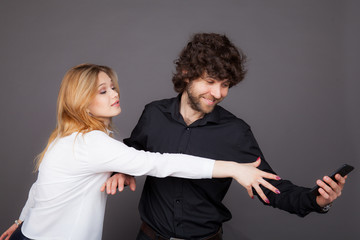 a young woman trying to take a phone from a man. Photo taken in studio on a gray background