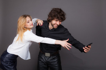 a young woman trying to take a phone from a man. Photo taken in studio on a gray background