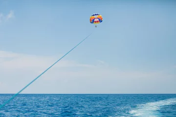 Cercles muraux Sports nautique Personnes volant sur un parachute coloré remorqué par un bateau à moteur
