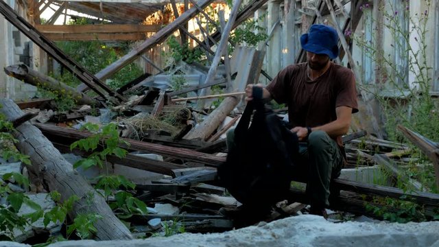 Tourist looks some thing in his bag and sits at ruins of a building at wasteland