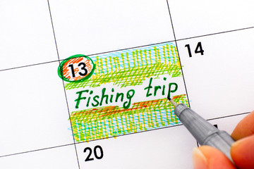 Woman fingers with pen writing reminder Fishing Trip.