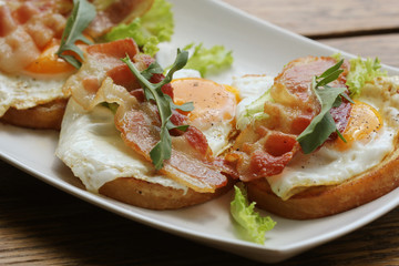 Bruschetta with rucola, chrispy bacon and poached egg served on white plate