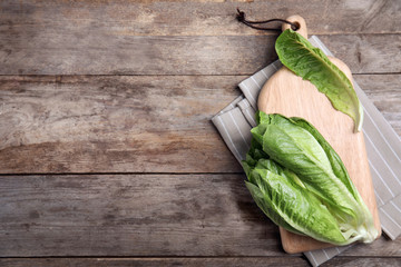 Board with fresh ripe cos lettuce on wooden background, top view