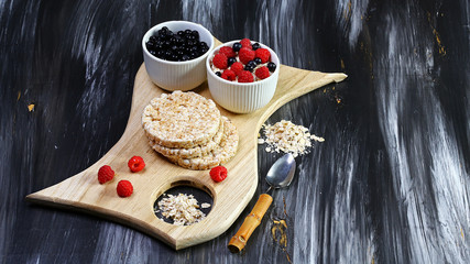 Healthy breakfast. Crispbread, raspberries and blueberries on the board, on the dark background. Copy space
