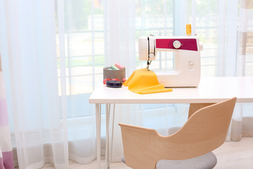Modern sewing machine on table near window indoors