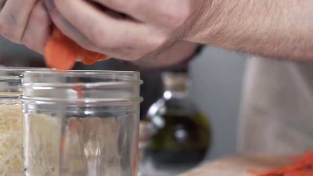 Tracking shot of chef scooping up fresh sliced carrots and dumping them into mason jar