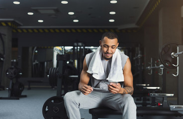 Fototapeta na wymiar Black bodybuilder using mobile phone at gym