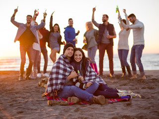 Obraz premium Couple enjoying with friends at sunset on the beach