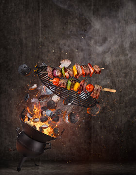 Kettle grill with hot briquettes, cast iron grate and tasty skewers flying in the air.