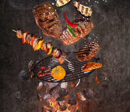 Kettle grill with hot briquettes, cast iron grate and tasty meats flying in the air.