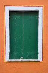 Closed window with green shutter on orange wall