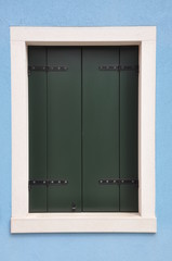 Closed window with green shutter on blue wall