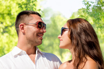 love, summer and relationships concept - happy smiling couple in sunglasses over green natural background