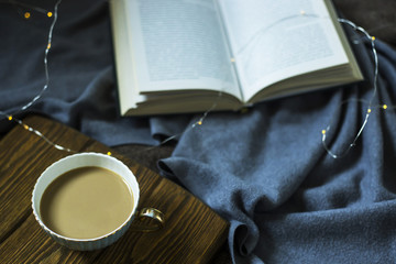 A cup of coffee with milk and a book on cozy domestic plohad. Time for rest in autumn or winter