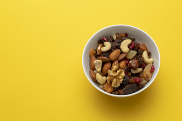 Mix of dried fruits and nuts in a bowl on a yellow background