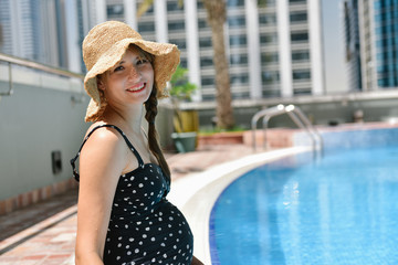 Beautiful young pregnant woman wearing swimsuit sitting in swimming pool.