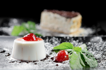 Photo of italian panna cotta dessert with strawberry sirup and mint leaf on the black wooden background.