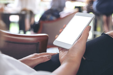 Mockup image of woman's hands holding white mobile phone with blank desktop screen while sitting in cafe