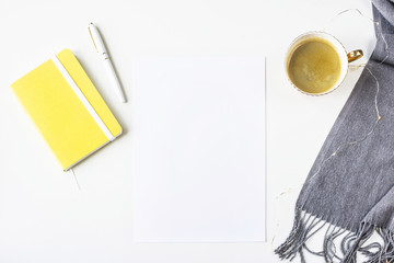 Autumn mock up on a white table next to a scarf, yellow notepad with a pen and a cup of coffee. Top view, flat lay. Copy space