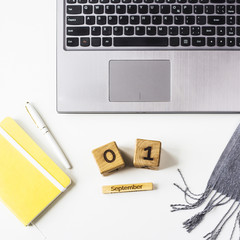 September 1 date on the wooden calendar. At the autumn workplace behind the computer, next to the scarf, glider and pen. Top view, flat lay