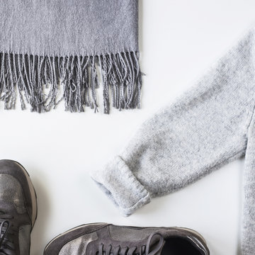 Gray with silver female sneakers, scarf and sweater on a white background. Autumn Fashion Concept. Top view, flat lay