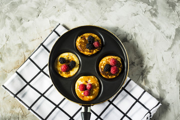 Pan with pancakes and berries of raspberries and blackberries on a checkered napkin on a gray table. Top view, flat lay