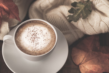 Hot coffee cappucino, blanket and autumn leaves on old wooden background. Seasonal relax concept