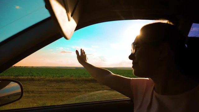 Teen Waves Her Hand In The Wind In car slow motion video. Young happy young girl drives a car a holds her hand out from the window. Road trip, travel and freedom concept lifestyle.