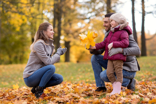 family, season and people concept - happy father and little daughter giving maple leaves to mother at autumn park